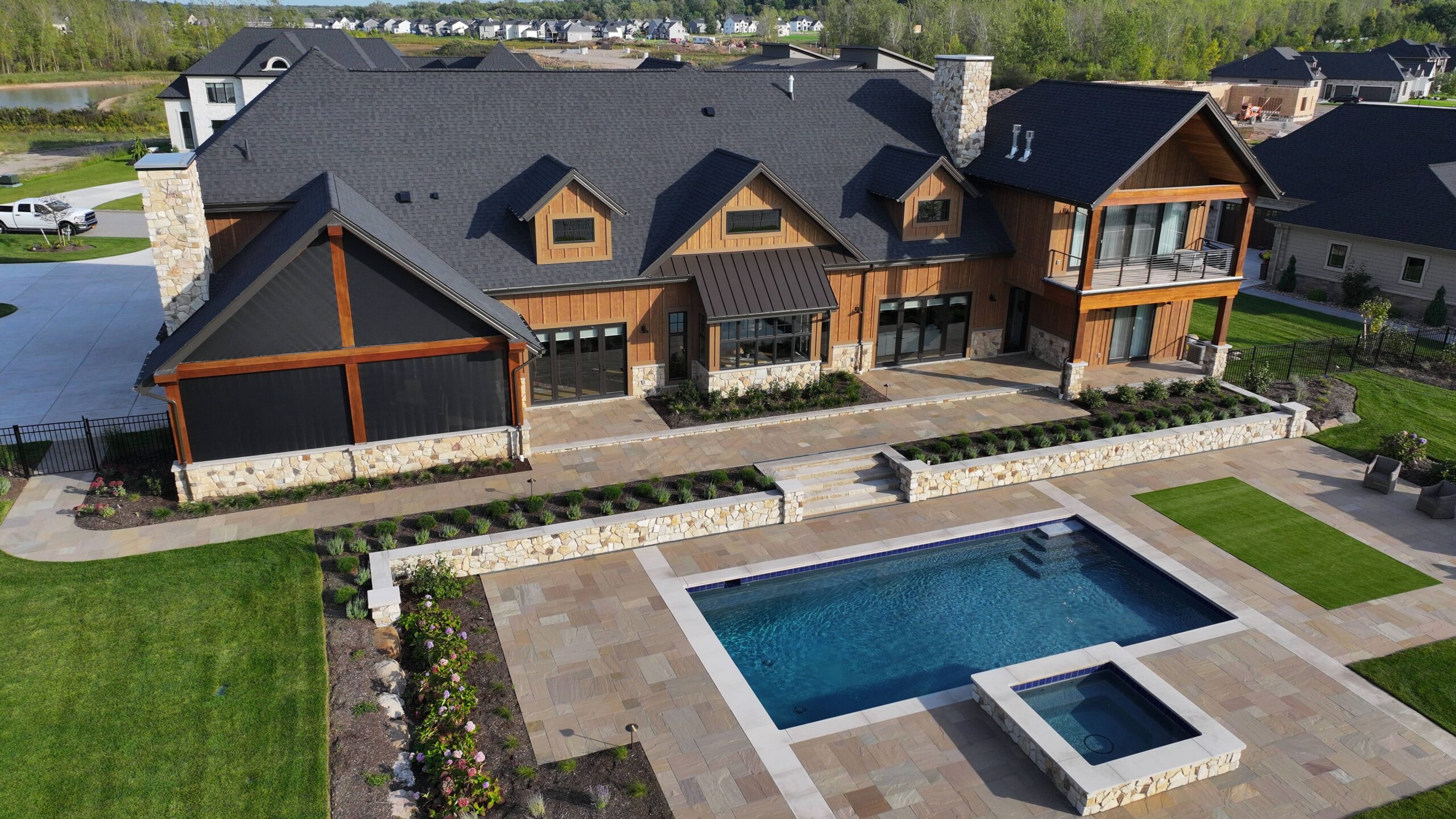 Complete luxury backyard renovation with multi-level natural stone patio, planted gardens, custom pool, and hot tub.