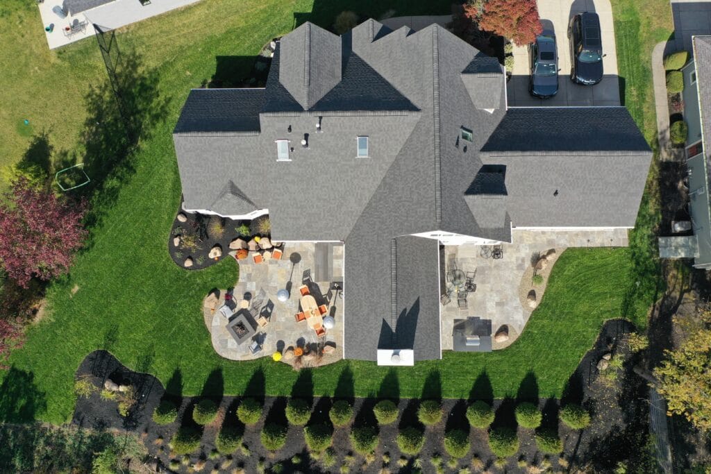 A n aerial view of a back yard with a patio built on either side of the rear wing of the house