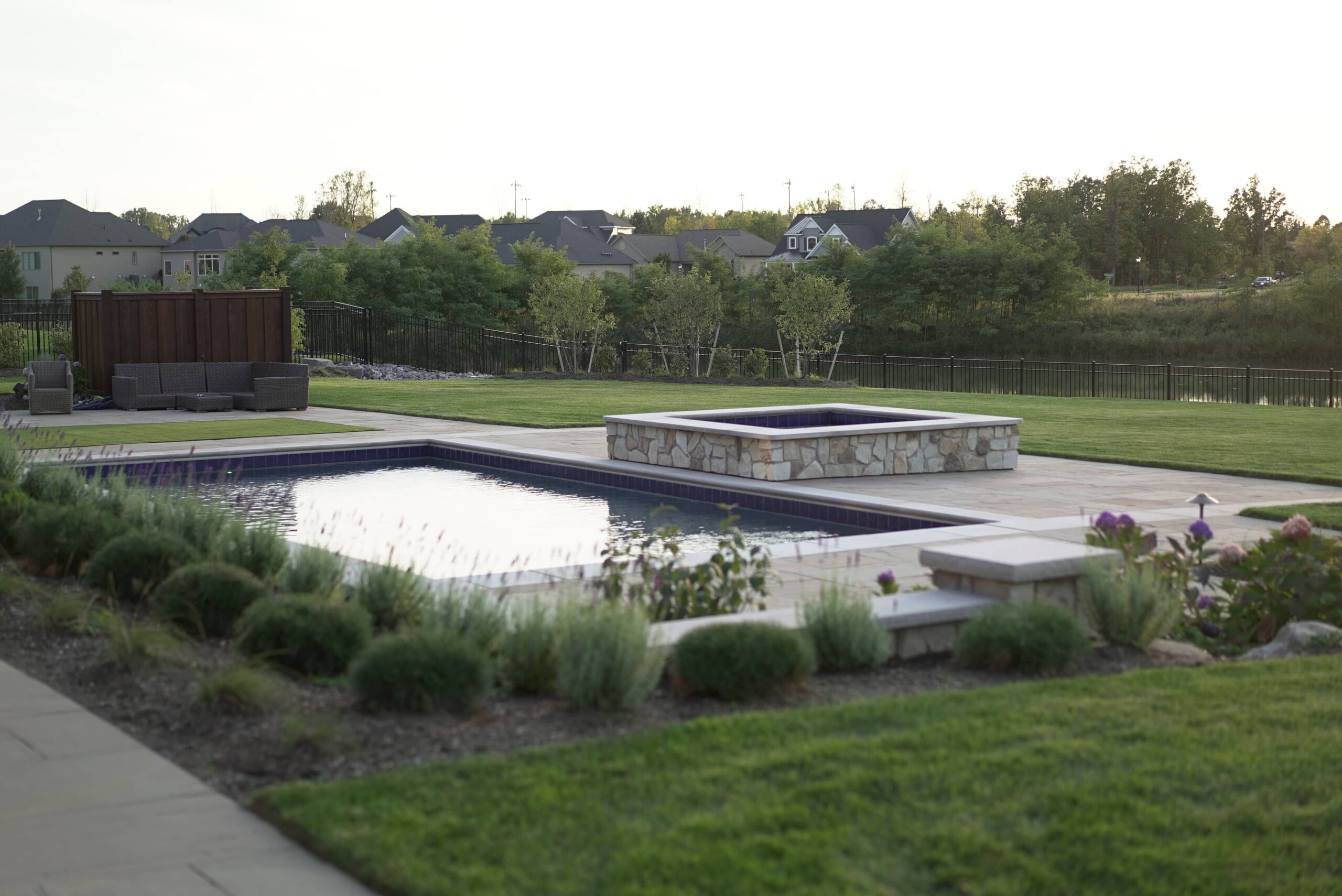Custom rectangular swimming pool with integrated hot tub and landscaped planting beds in Clarence New York