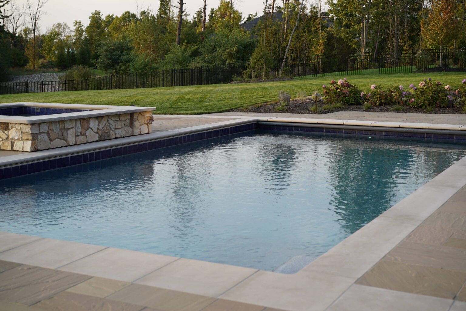 Custom rectangular swimming pool with integrated hot tub in landscaped backyard in Clarence New York