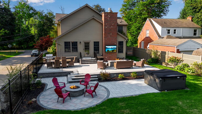 Multi-level backyard patio with fire pit seating, outdoor lounge area, hot tub, and landscaped garden.
