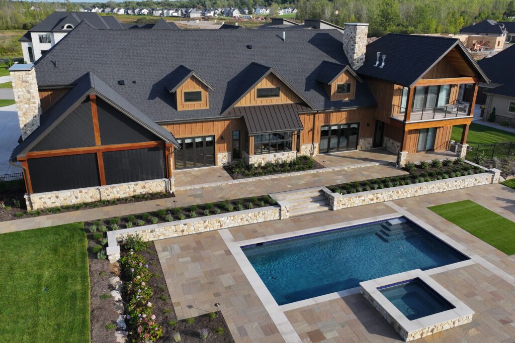 Aerial view of a luxury home with custom swimming pool, raised spa, stone patio, and landscaped outdoor living areas.